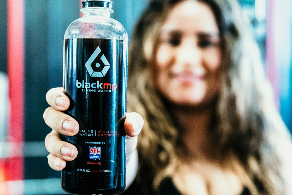 Woman holding BlackMP Living Water bottle made with Fulvic Humic mineral powder, featuring probiotics and NFL Alumni logo.